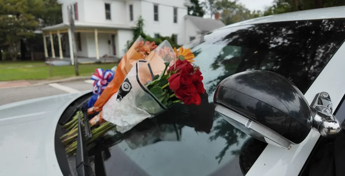 Flowers on a police car and half-staff flags honoring Denton Police Chief George Bacorn