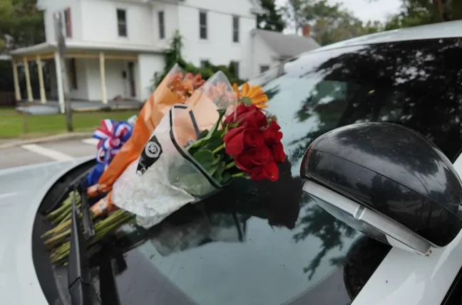 Flowers on a police car and half-staff flags honoring Denton Police Chief George Bacorn